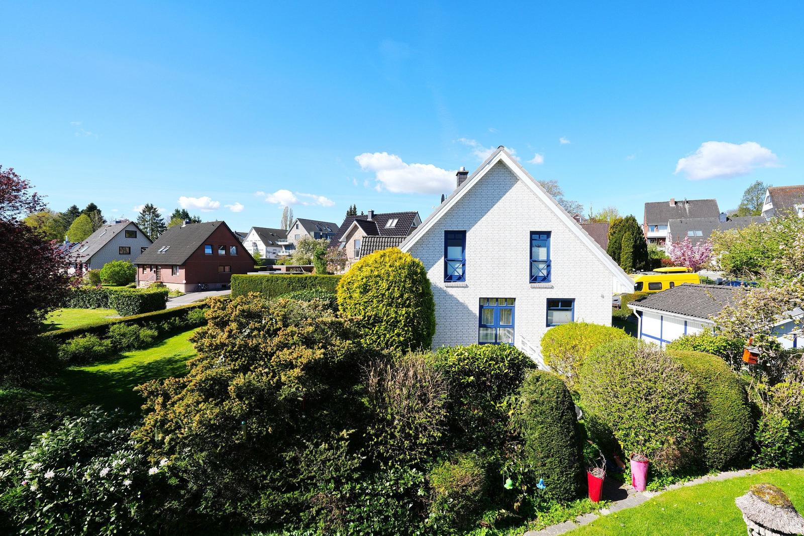 Weißes Haus mit blauen Fenstern und grünem Garten unter blauem Himmel.
