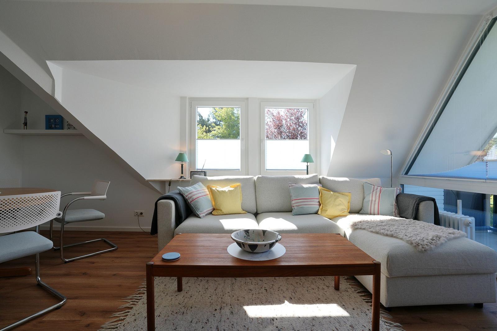Wohnzimmer mit Sofa, Couchtisch und Fenstern. Holzboden und Dachschrägen.