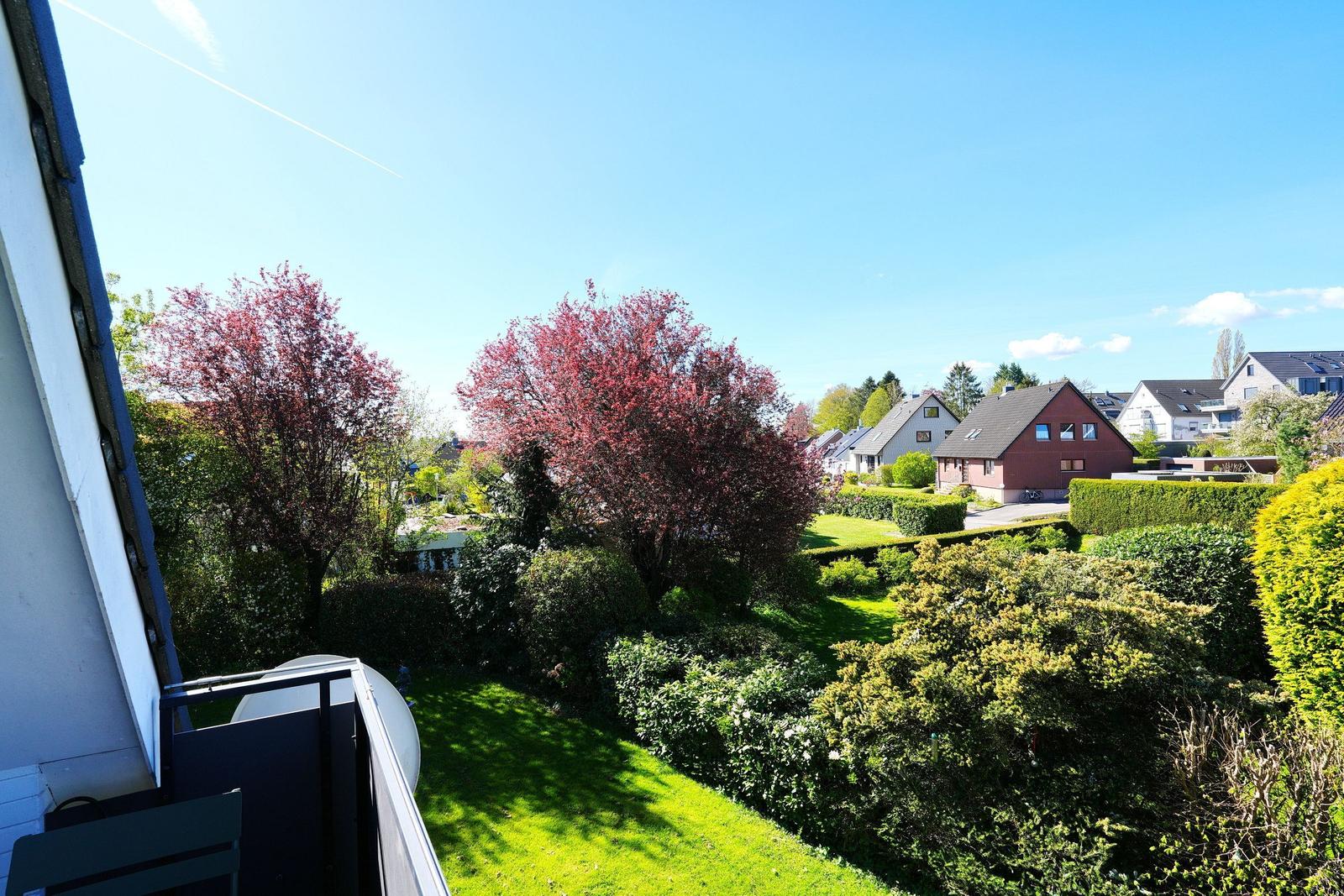 Blick vom Balkon auf grünen Garten mit Bäumen und Häusern im Hintergrund.