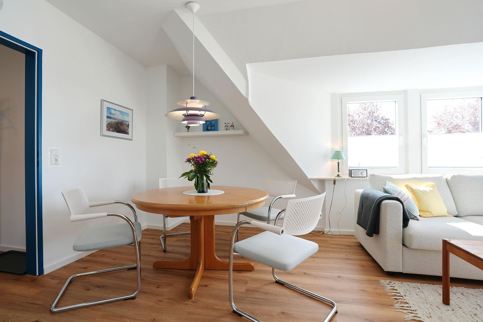 Esszimmer mit Tisch, Stühlen und Sofa. Holzboden und Dachschräge sichtbar.