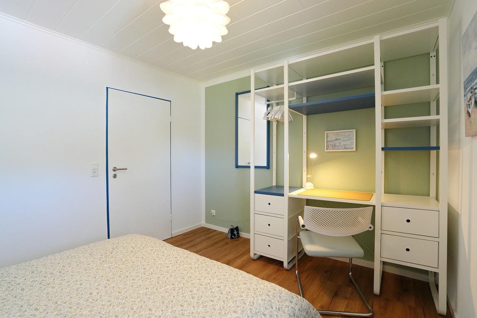 Schlafzimmer mit Bett, Schreibtisch und Kleiderschrank. Holzboden und helle Wände.