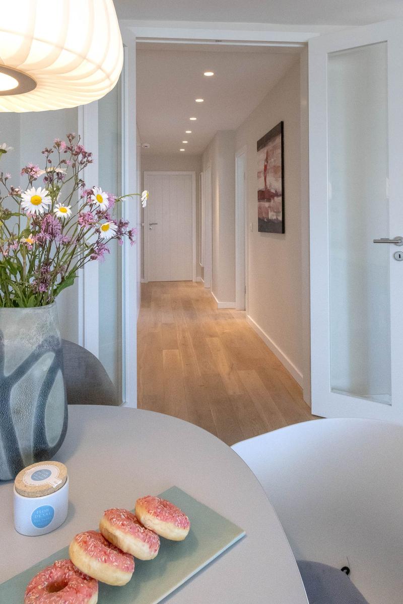 Tisch mit Donuts und Blumen, Blick in einen Flur mit Holzboden und Wandbild.