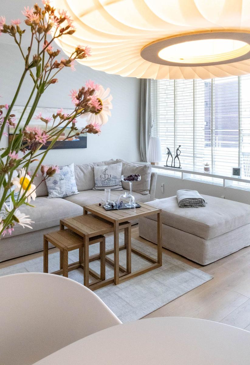 Wohnzimmer mit Sofa, Tisch und Fenster. Blumen im Vordergrund.