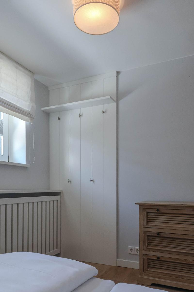 Schlafzimmer mit weißem Schrank, Holzkommode und Fenster mit Rollladen.