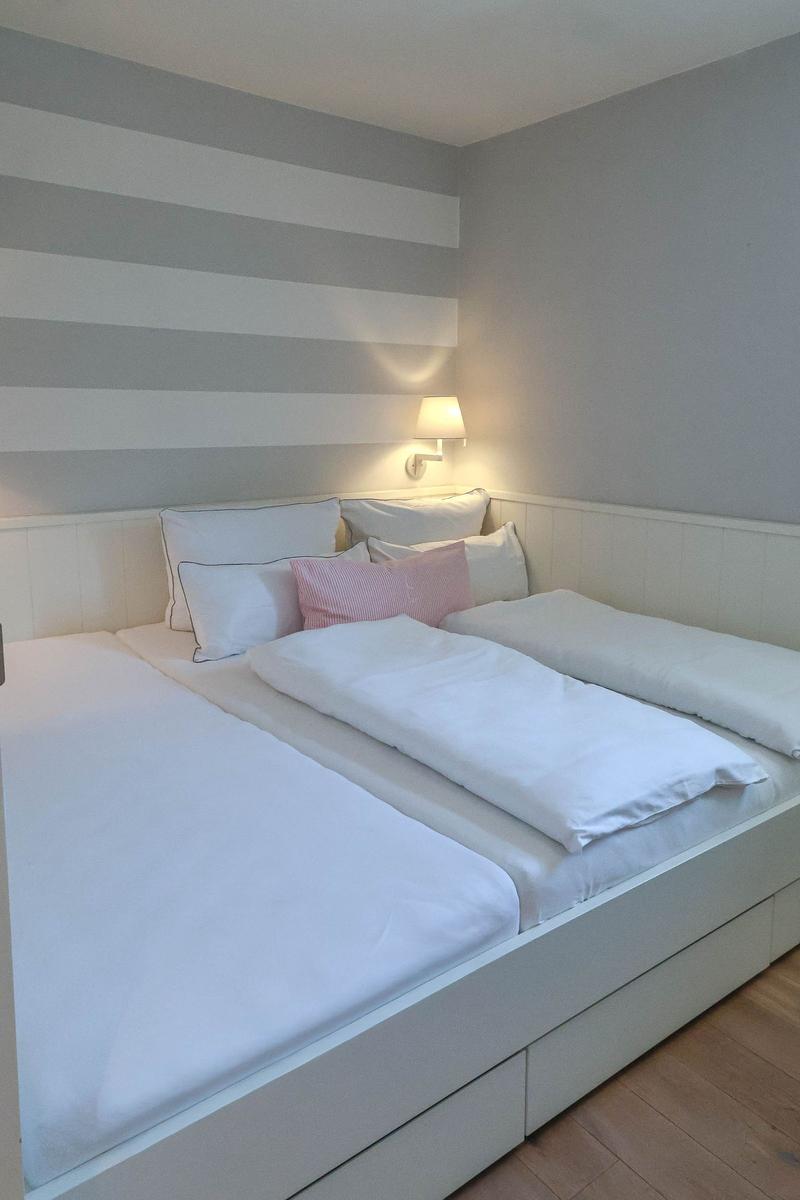Schlafzimmer mit Doppelbett, gestreifter Wand und Wandlampe.