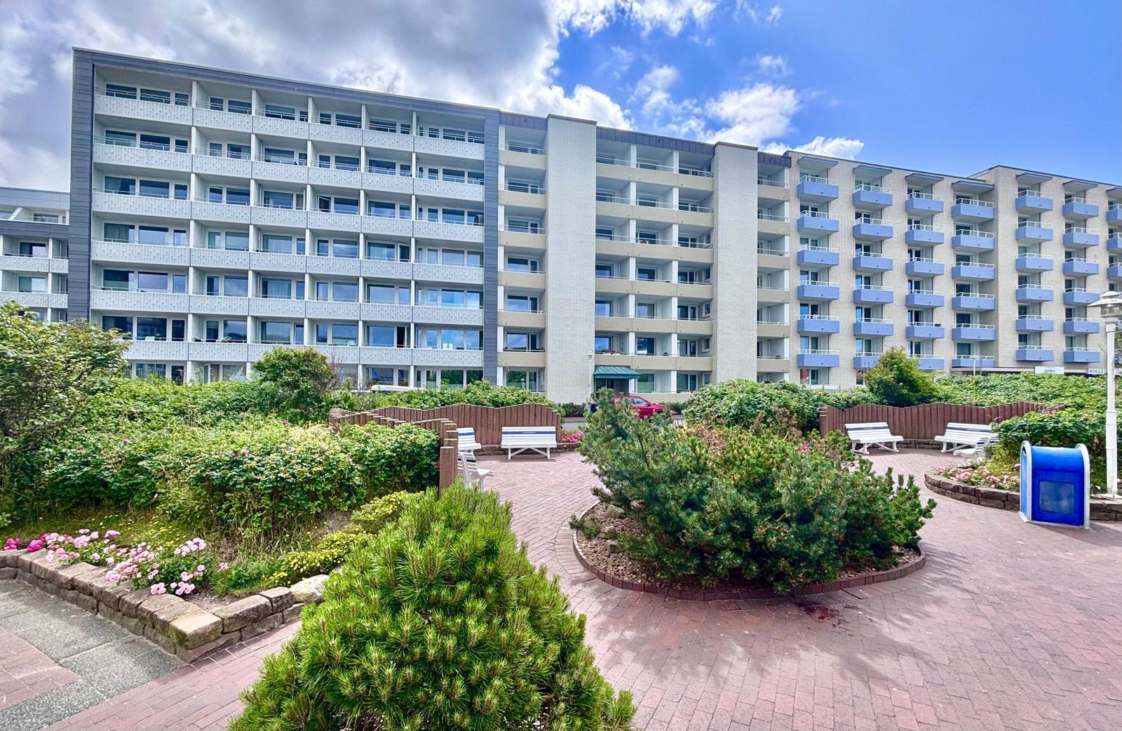 Hochhaus mit Balkonen, gepflasterter Gartenbereich und Sitzgelegenheiten.