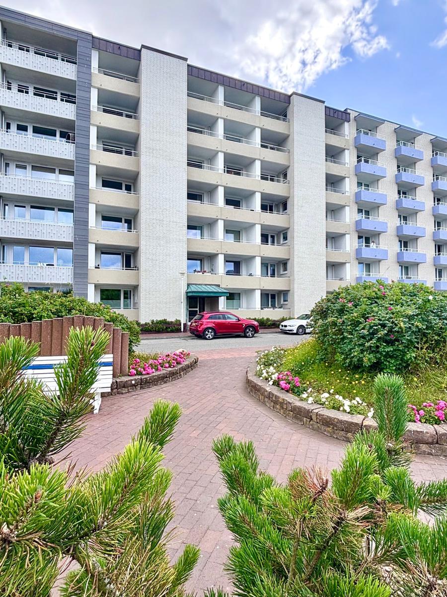 Hochhaus mit Balkonen, gepflasterter Weg und Blumenbeete im Vorgarten.