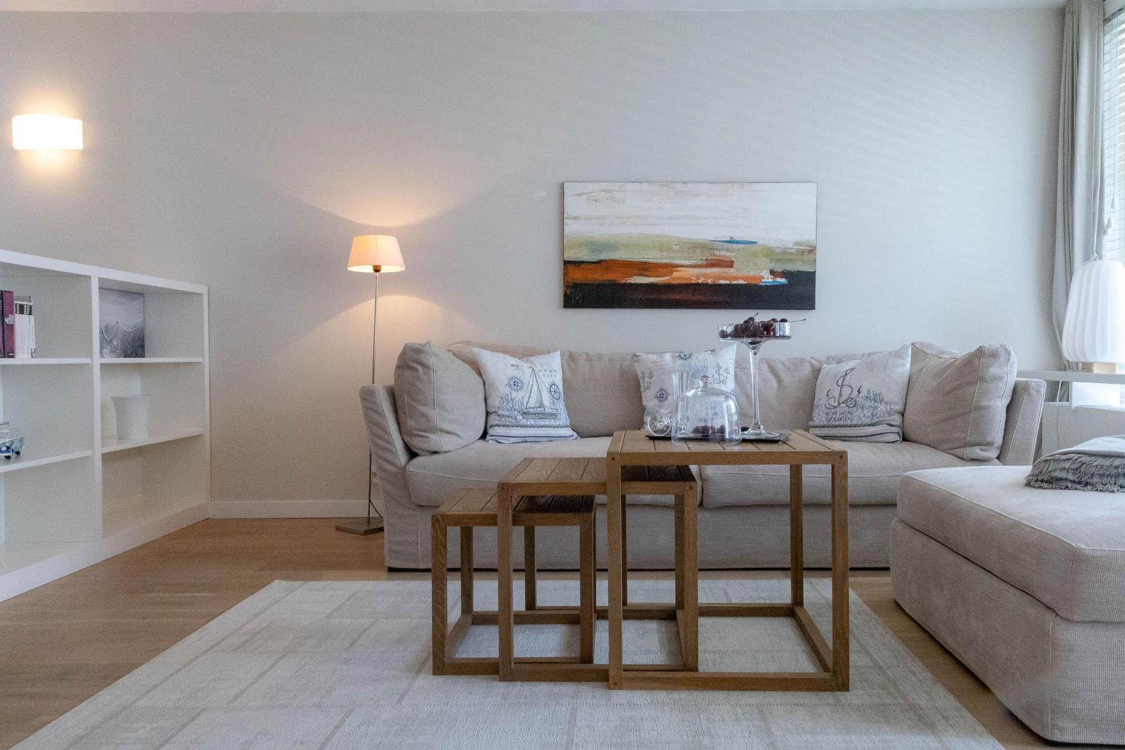 Wohnzimmer mit Sofa, Couchtisch und Wandbild. Holzboden und Bücherregal sichtbar.