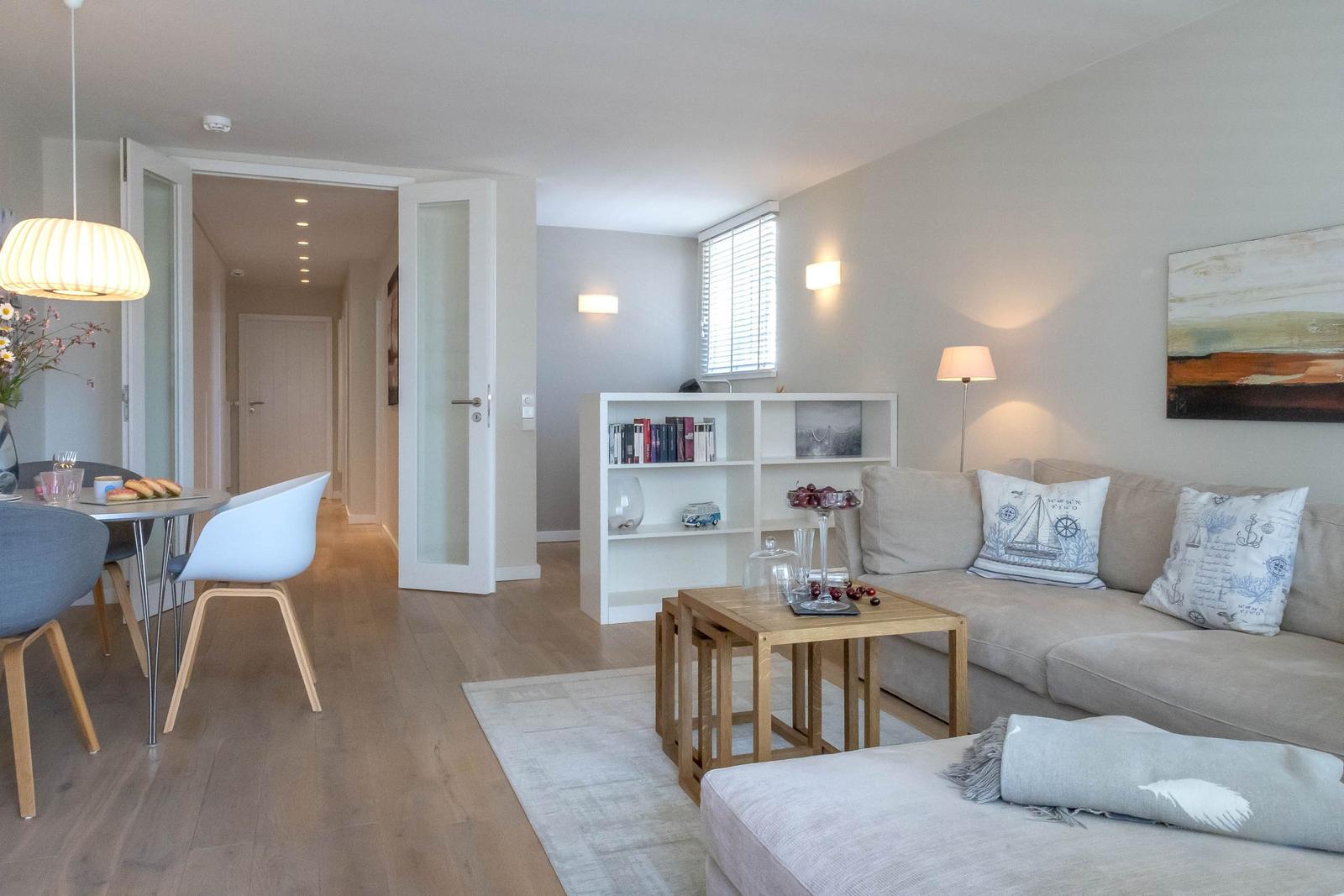 Wohn- und Essbereich mit Sofa, Tisch und Bücherregal. Holzboden und moderne Einrichtung.