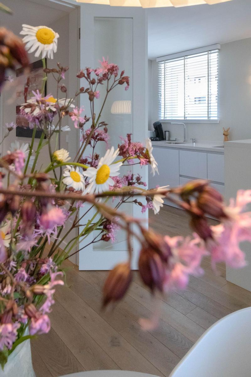 Ein Raum mit Holzboden, weißer Küchenzeile und Blumen im Vordergrund.