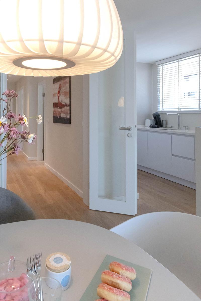 Essbereich mit Tisch, Donuts und Lampe. Küche mit weißen Schränken und Fenster.