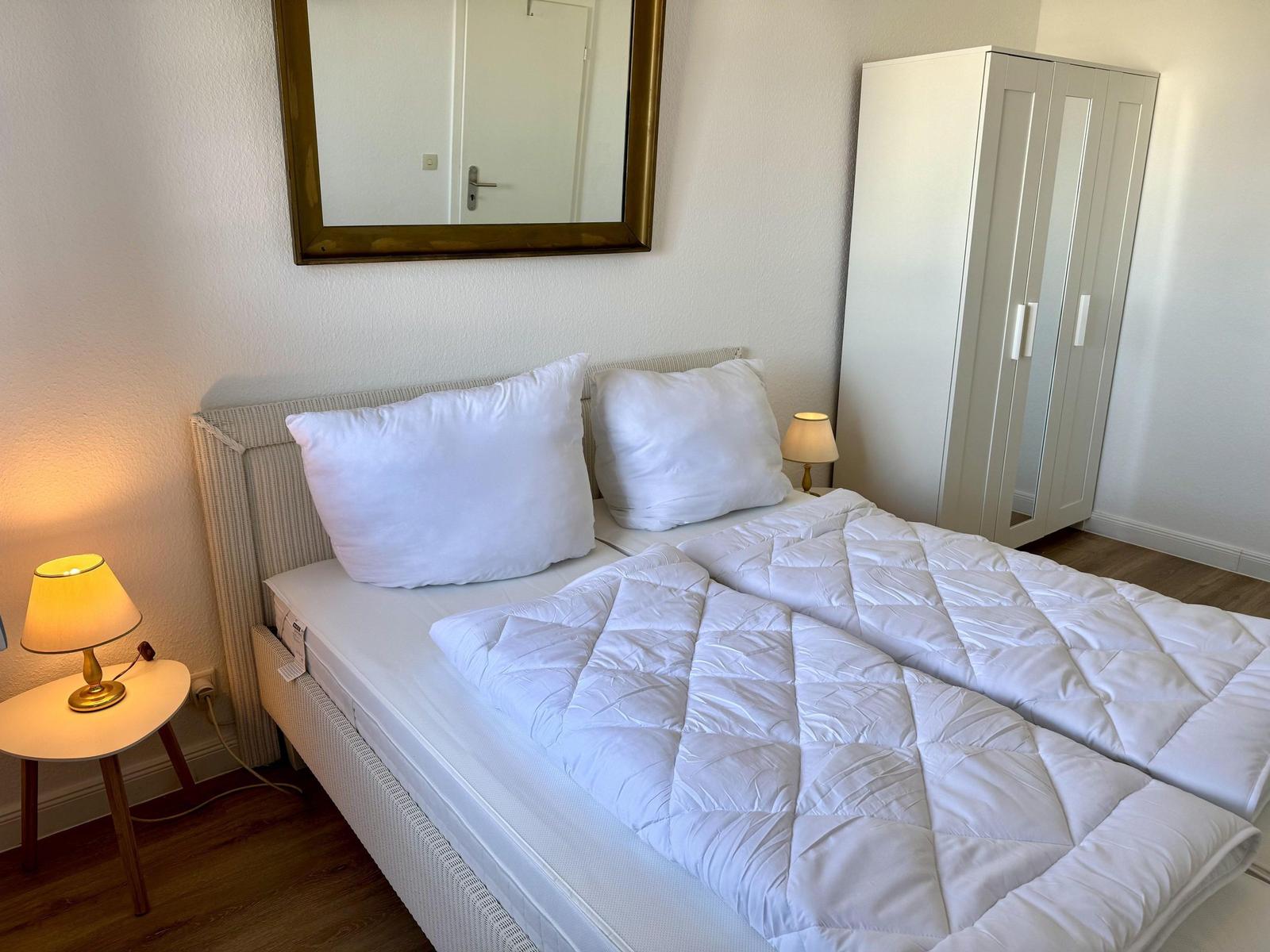 Schlafzimmer mit Bett, Nachttisch, Spiegel und Kleiderschrank.