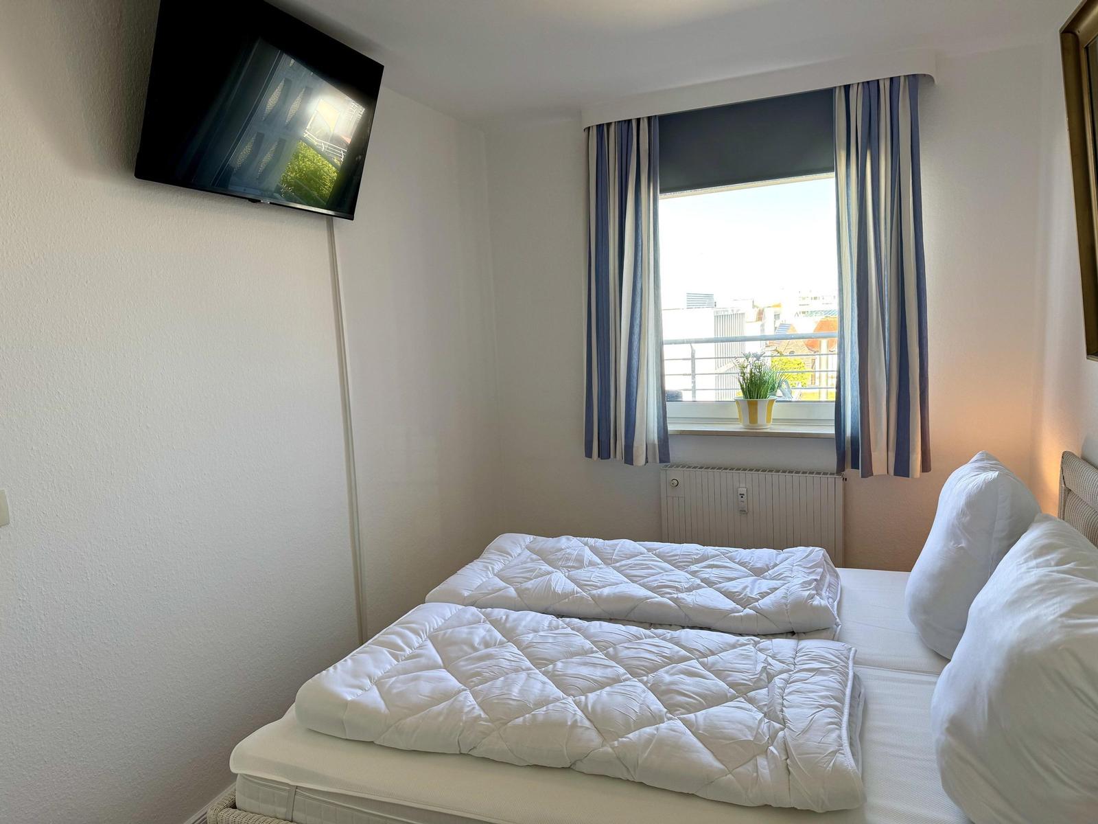 Zimmer mit Doppelbett, Fenster mit Blick und Wand-TV.