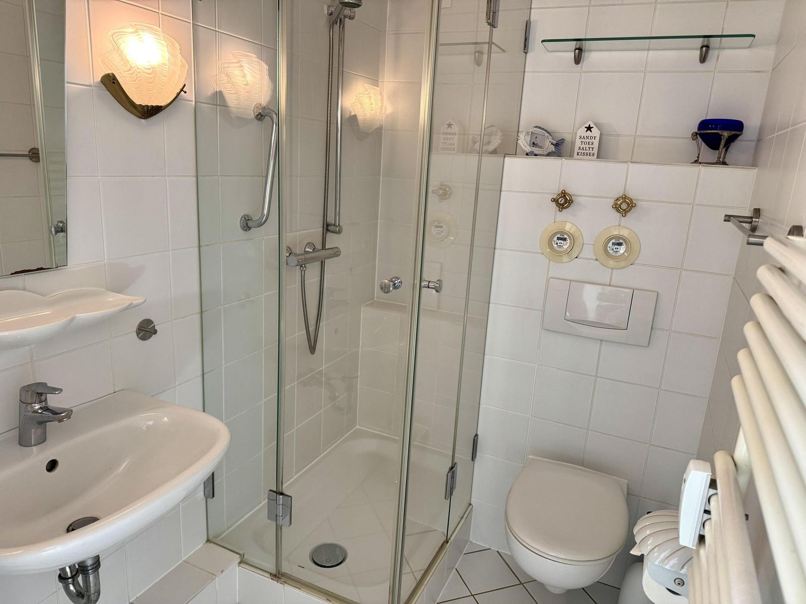 Badezimmer mit Dusche, Waschbecken und Toilette. Weiße Fliesen und Glaswand.