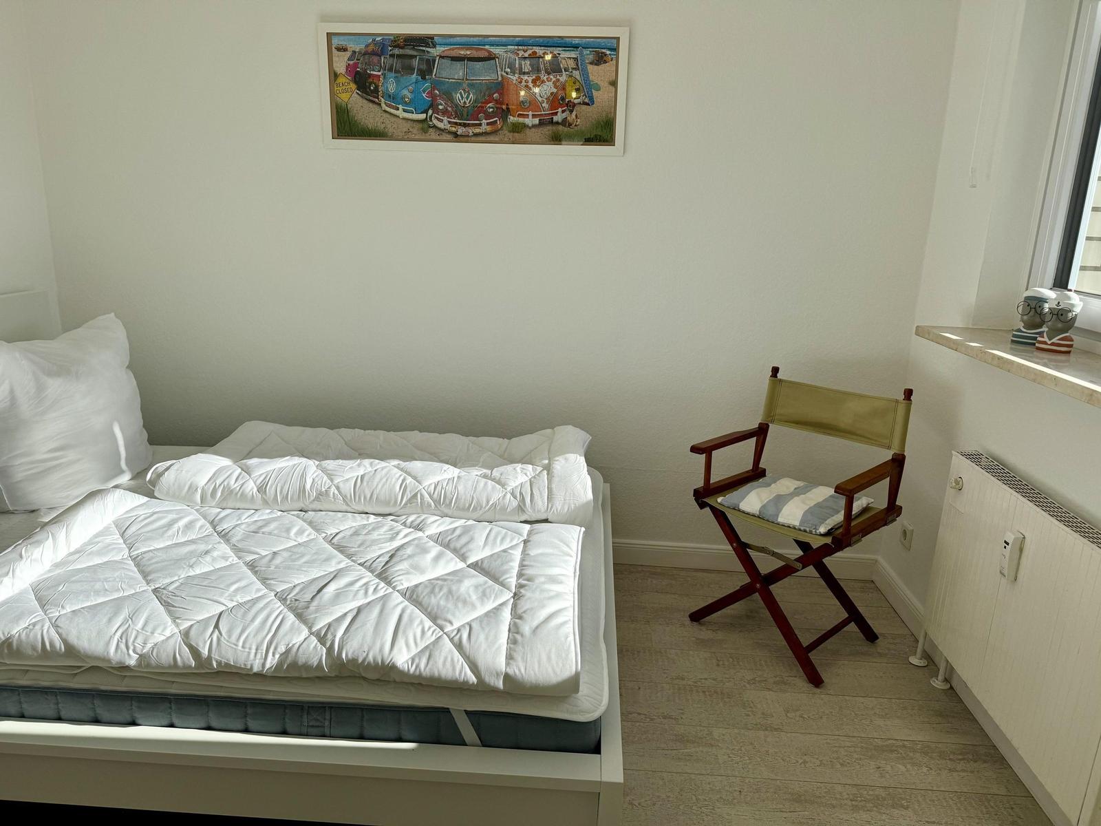 Schlafzimmer mit Bett, Stuhl und Wandbild von VW-Bussen.