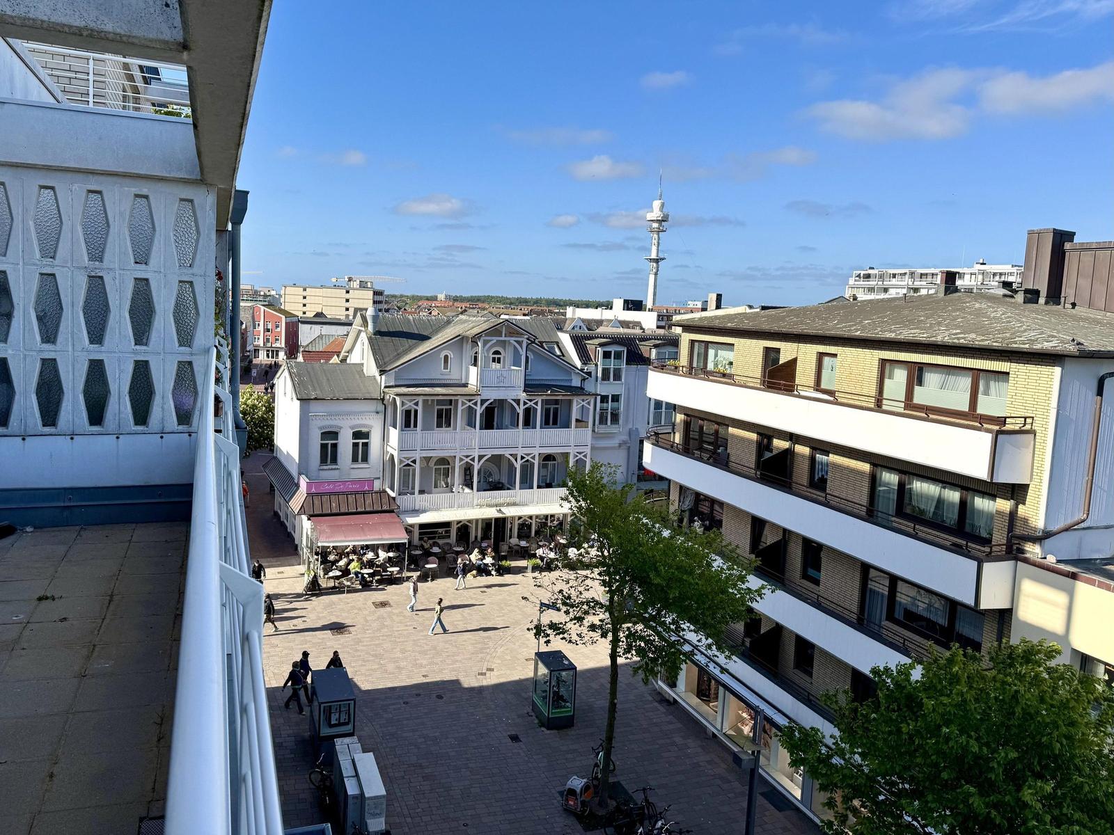 Blick auf einen Platz mit Gebäuden und einem Turm unter blauem Himmel.