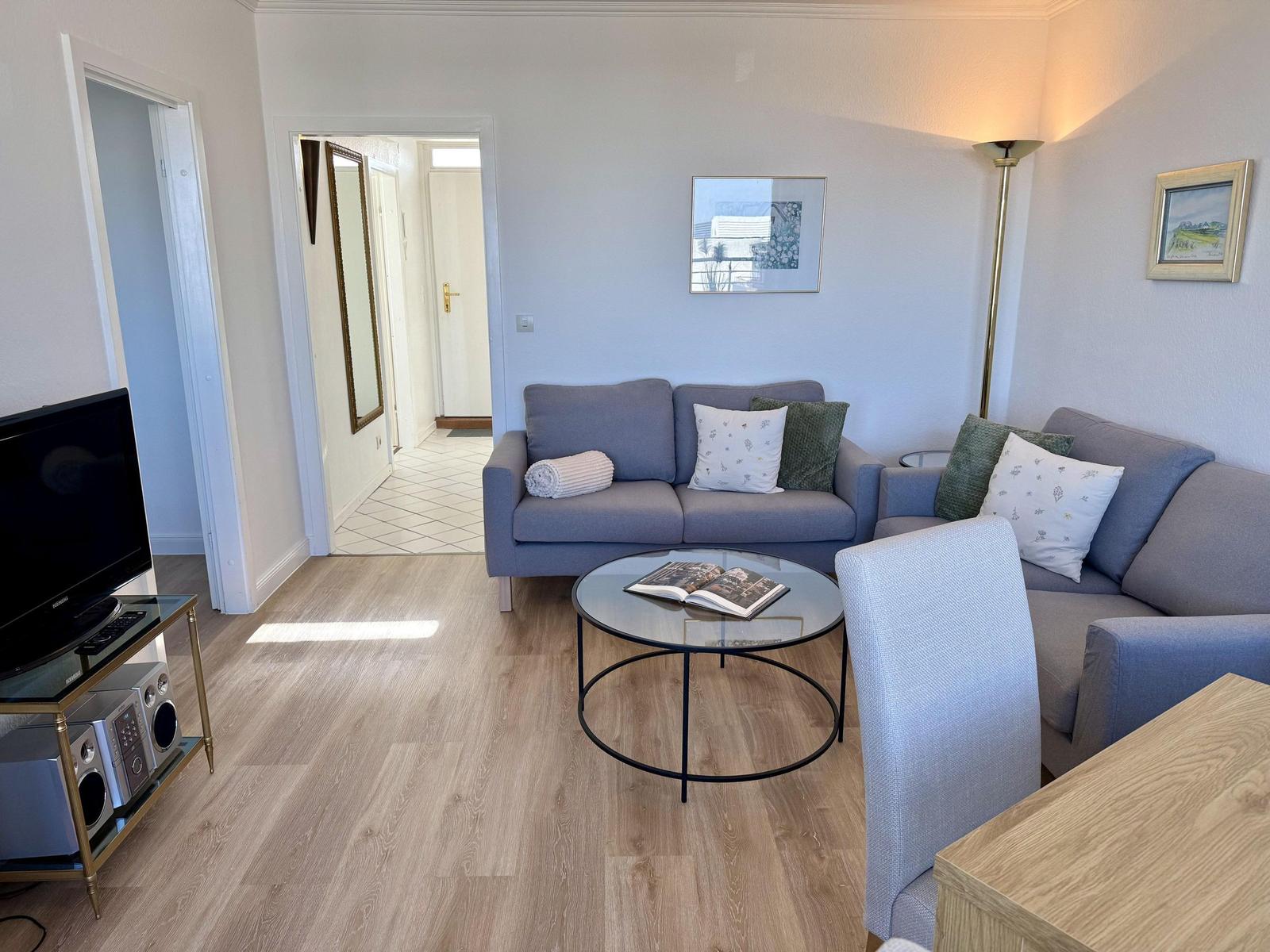Wohnzimmer mit Sofa, Glas-Tisch und Fernseher auf Metallgestell.