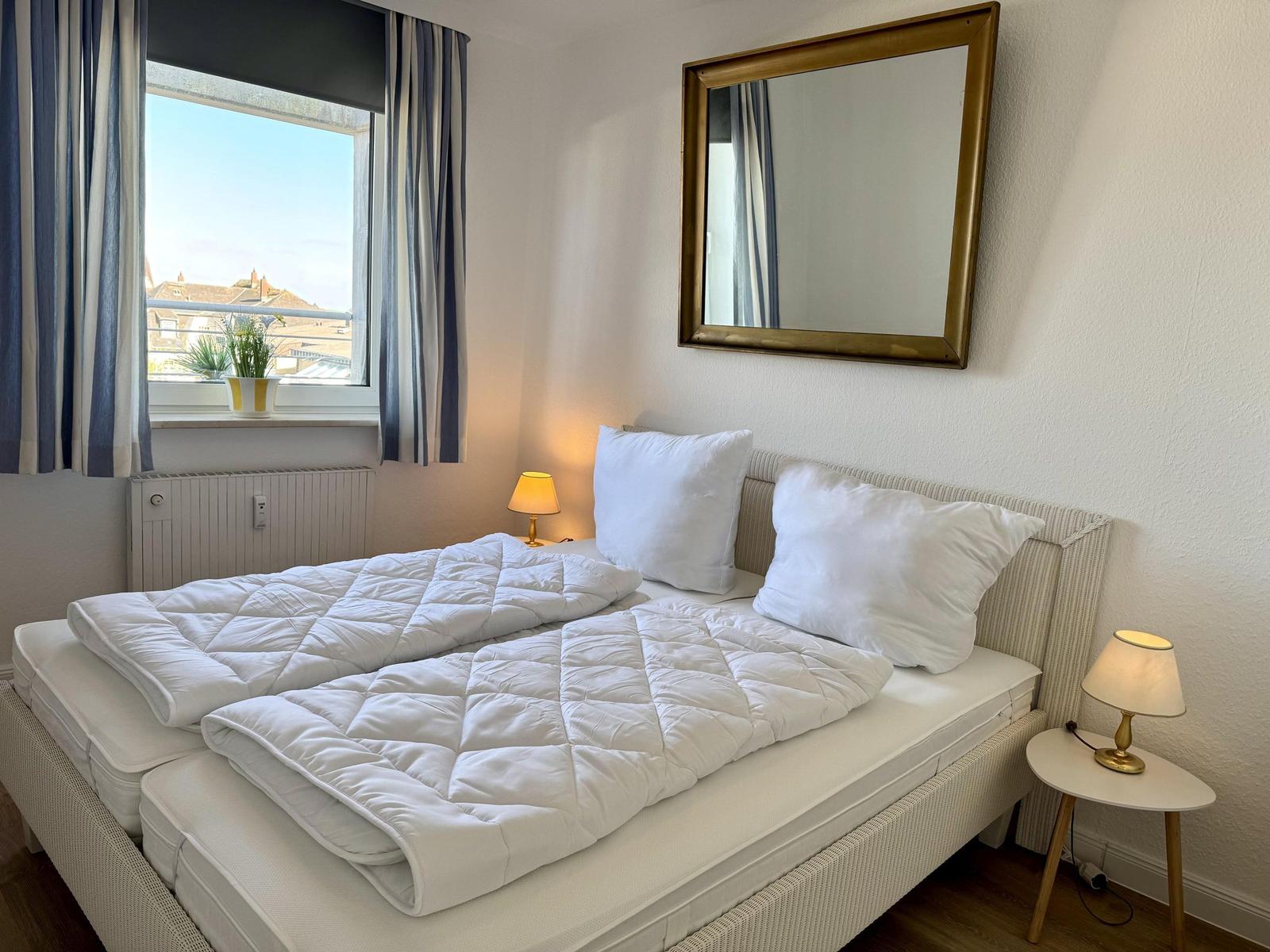 Schlafzimmer mit Doppelbett, Fenster, Spiegel und Nachttischlampen.
