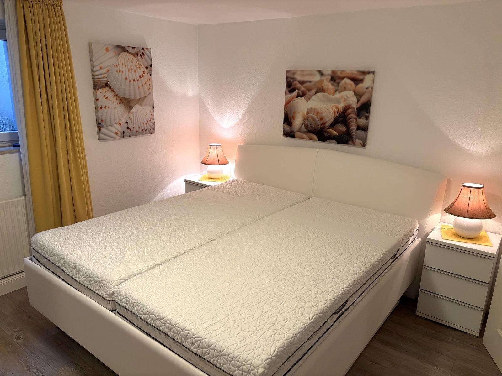 Schlafzimmer mit Doppelbett, zwei Nachttischen und Meeresmuschelbildern an den Wänden.