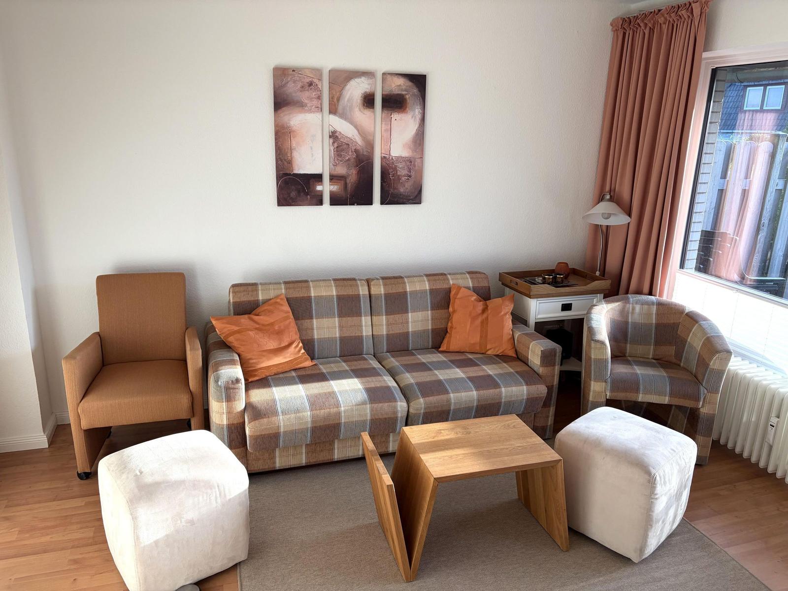 Wohnzimmer mit Sofa, Sessel und Tisch. Wandbild und Fenster mit Vorhängen.