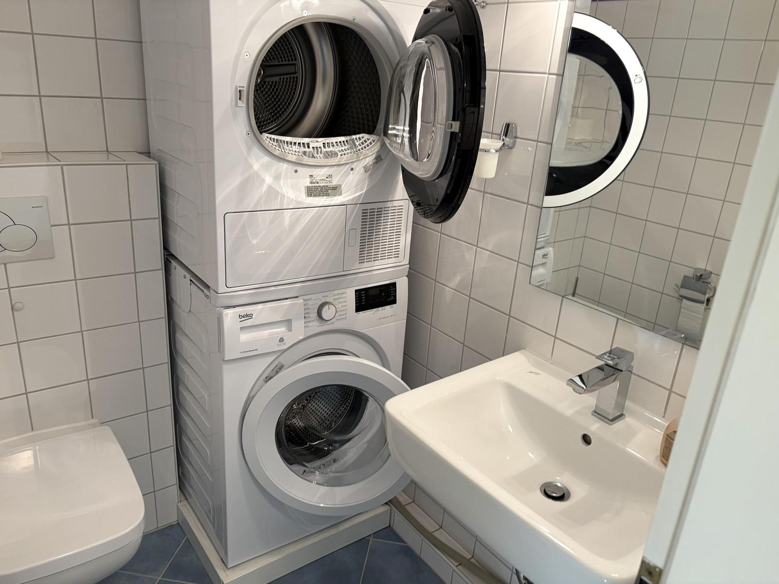 Waschmaschine und Trockner in einem Raum mit Waschbecken und Spiegel.