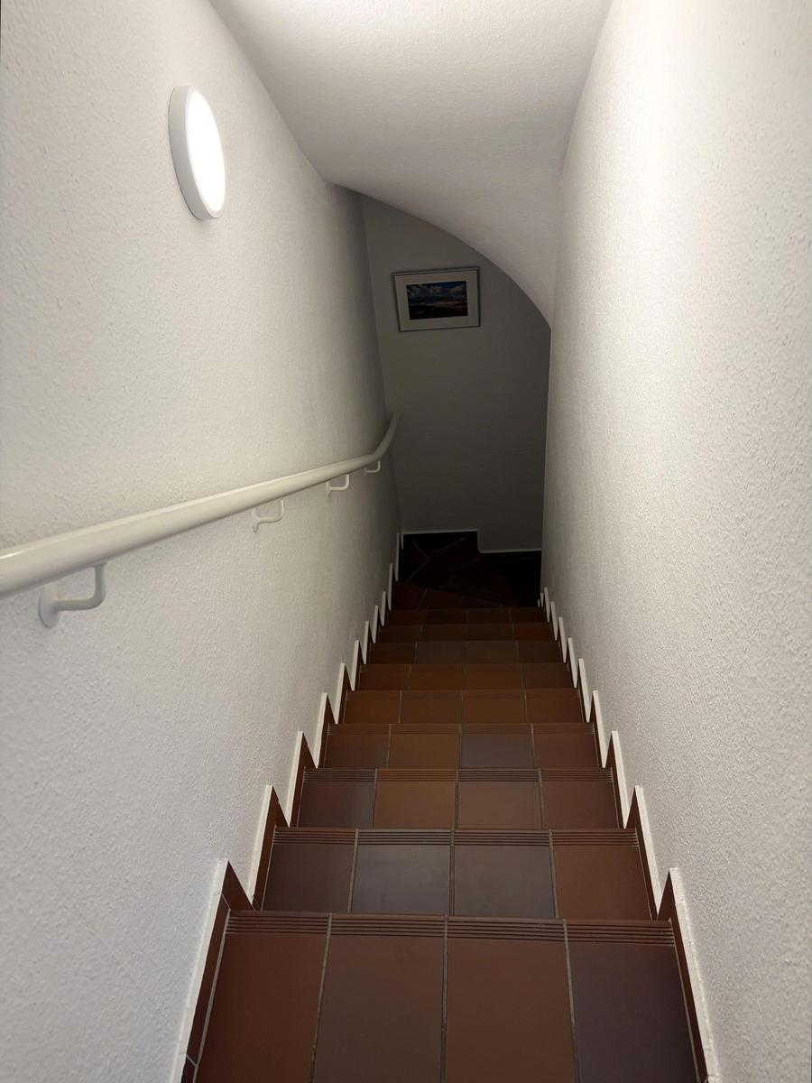Treppe mit braunen Fliesen und weißer Handlaufwand, Wandbeleuchtung und Bild an der Wand.