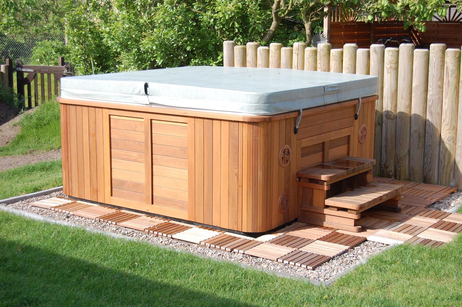 Ein Whirlpool mit Holzrahmen und Auflage auf einer Terrasse im Garten.