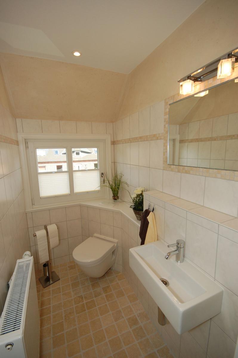Badezimmer mit Toilette, Waschbecken und Fenster. Fliesenwand und Boden.