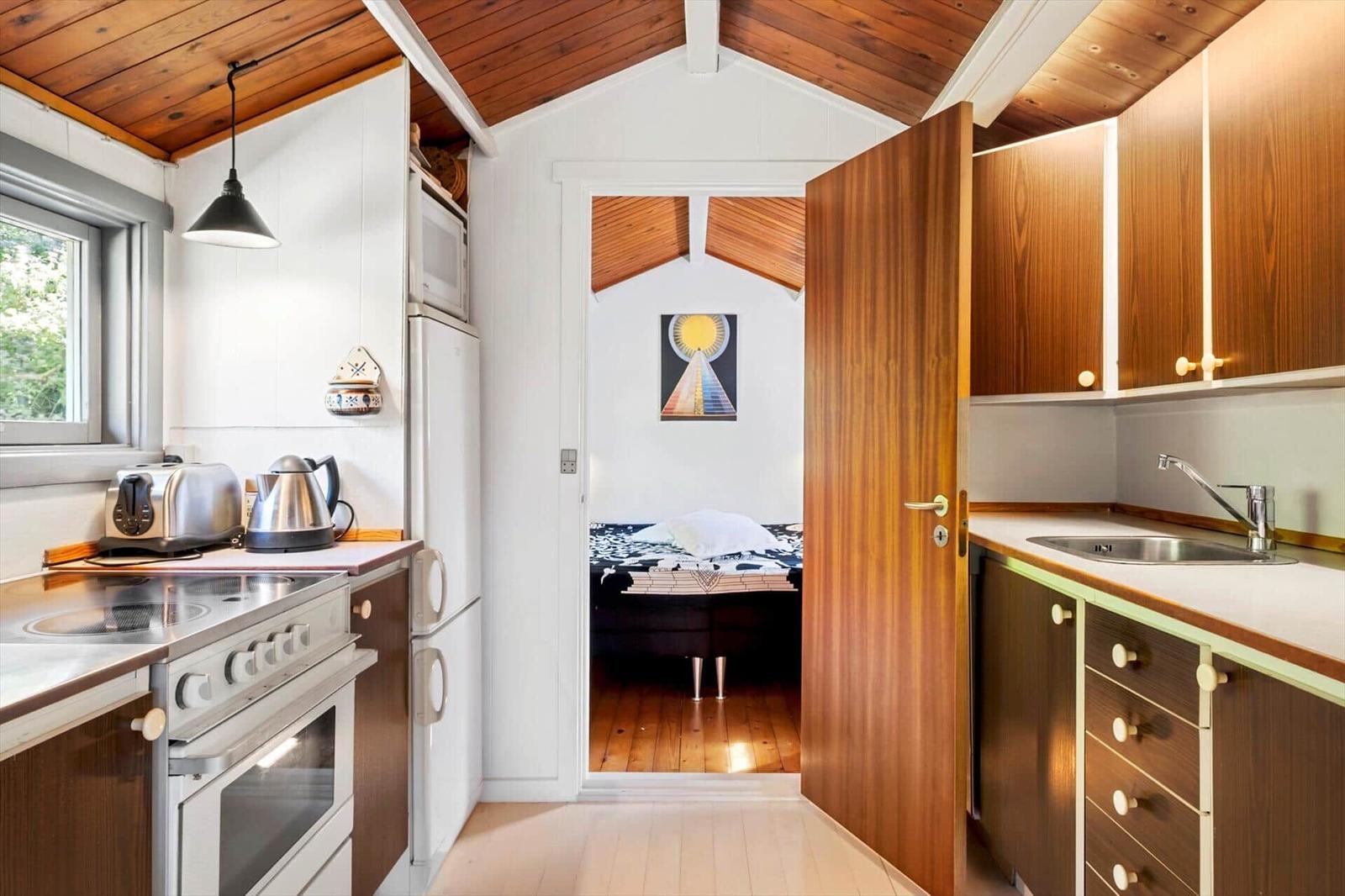 Kitchen with wooden ceiling and view into bedroom with bed and wall art.