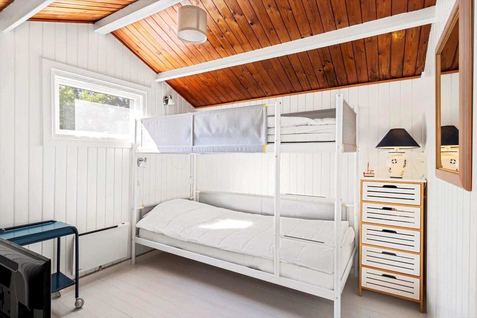Room with bunk bed, dresser, and window. Wooden ceiling and white walls.
