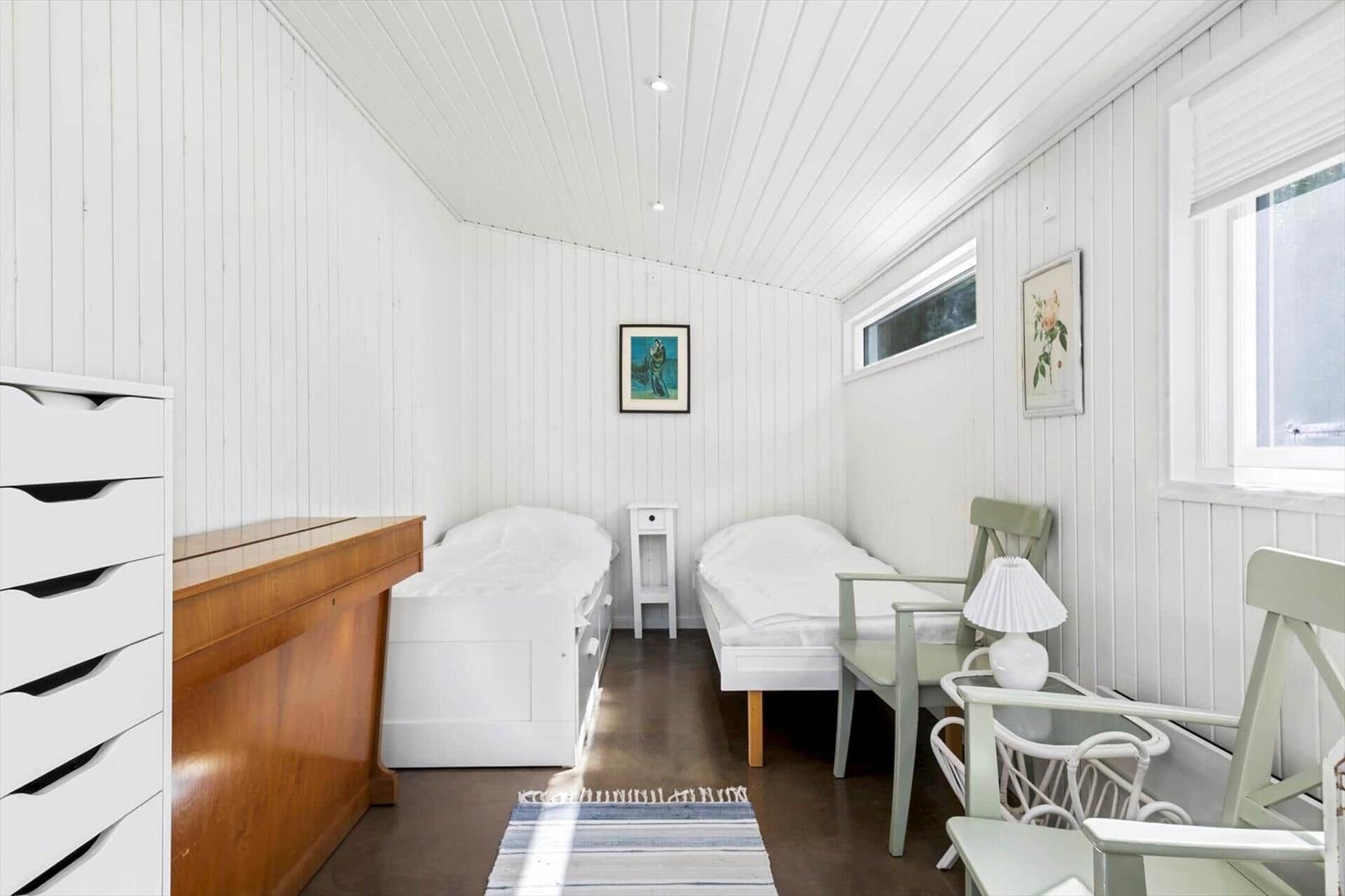 Two beds, a dresser, chairs, and windows in a room with white walls.