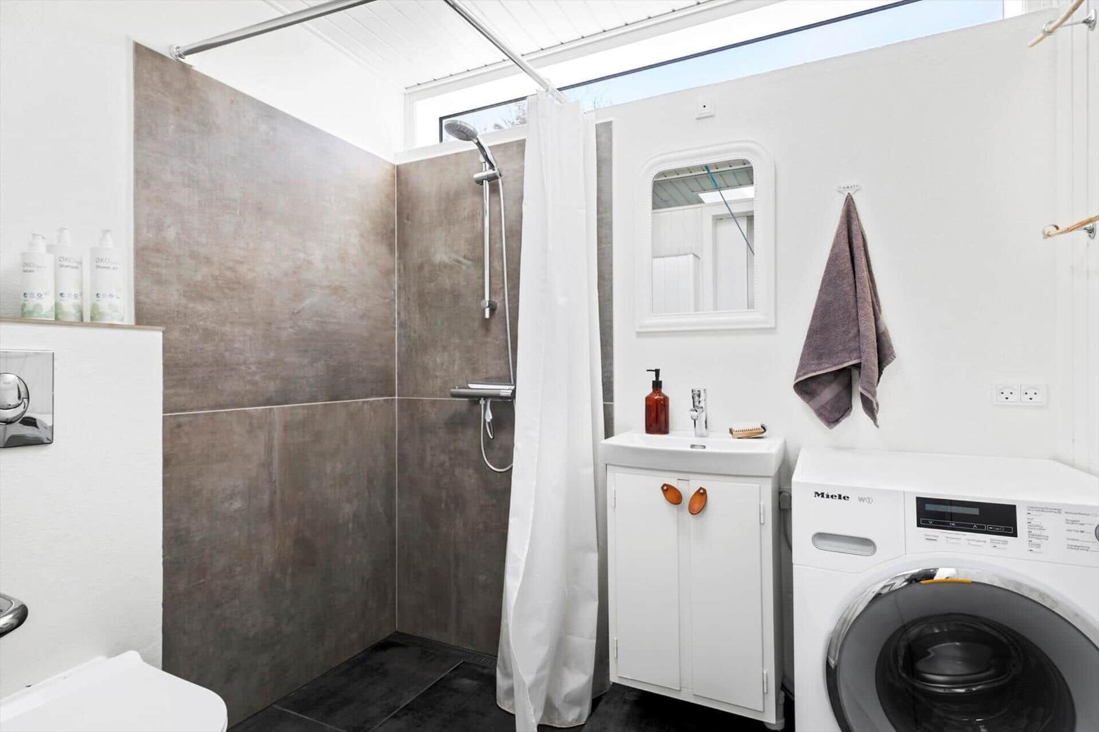 Shower with curtain, sink and washing machine against white wall.