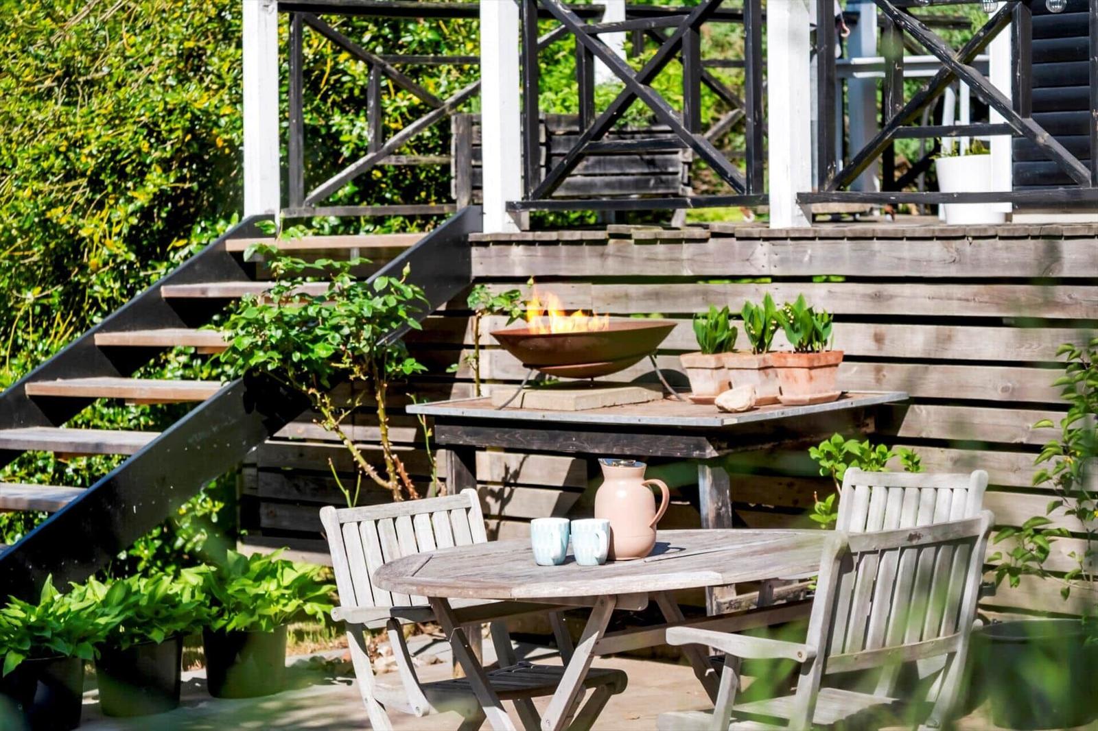 Wooden table with chairs, fire bowl, and plants on terrace.