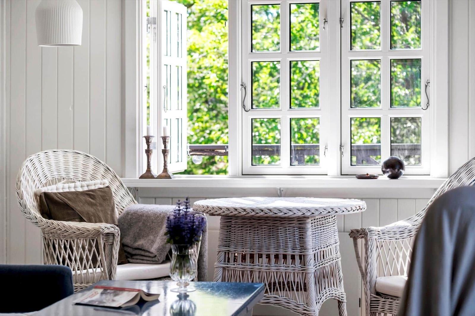 Living area with white wicker furniture and view of green trees through windows.