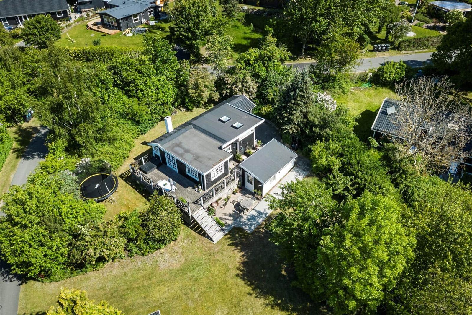 House with terrace, garden, and trampoline surrounded by trees.
