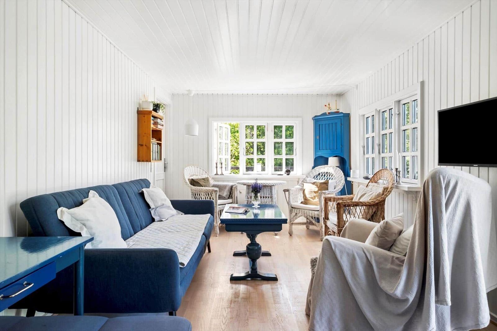 Living room with blue sofa, wicker chairs, and wooden floor. Windows with view of greenery.