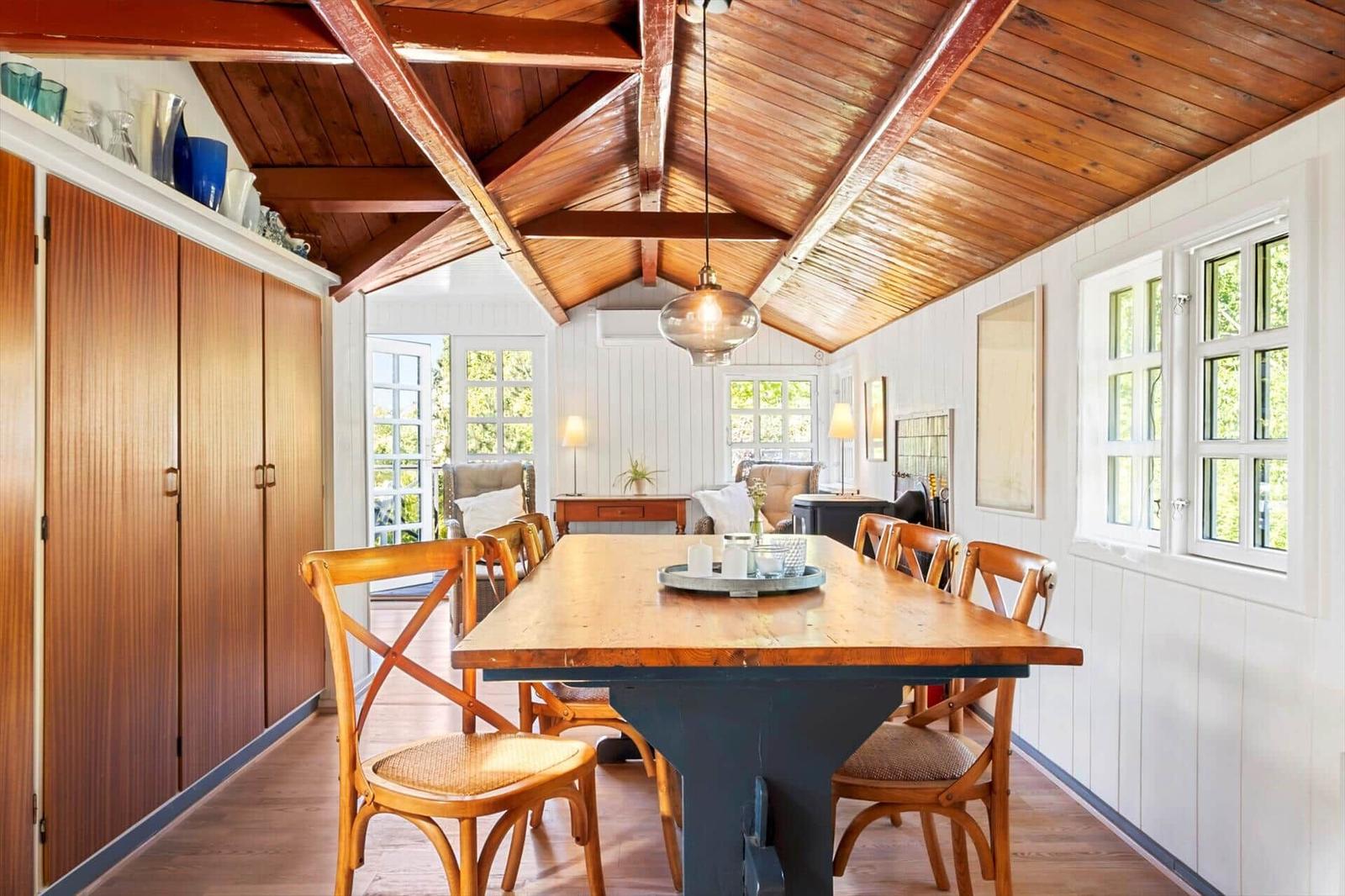 Dining room with wooden table, chairs, and high ceiling with beams.