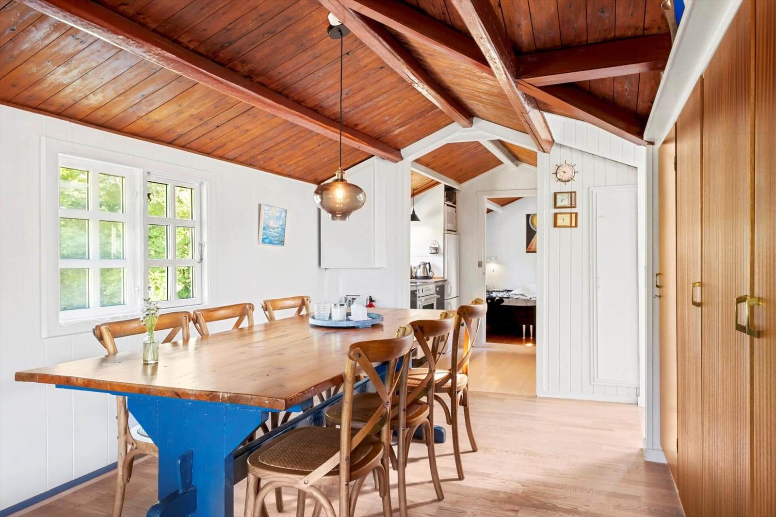 Dining area with wooden table, chairs, and view into the kitchen.