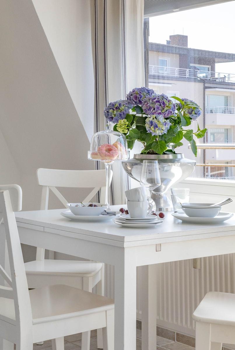Esstisch mit Stühlen, Blumen und Geschirr vor Fenster
