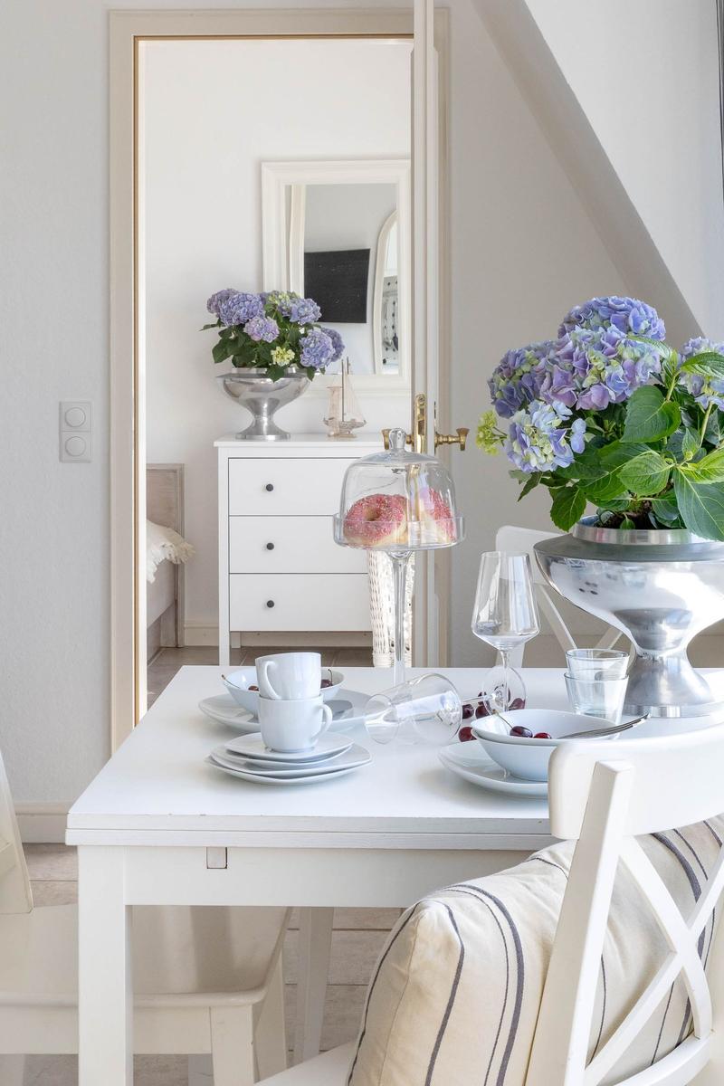 Esstisch mit Stühlen, Blumen und Geschirr. Im Hintergrund Schrank und Spiegel.