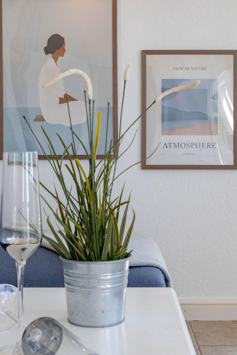 Auf Tisch steht Pflanze in Metalltopf, daneben Weinglas. Wand mit Bildern.