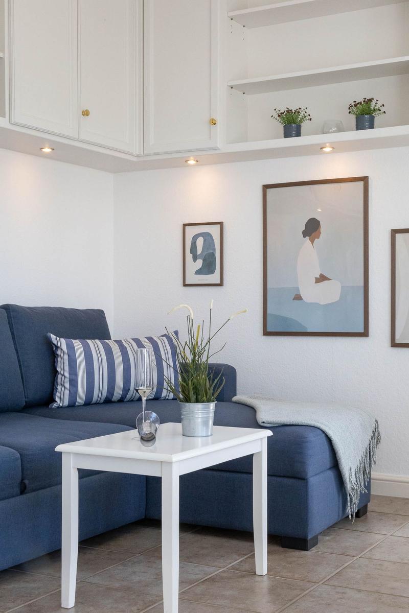 Ein Wohnzimmer mit blauem Sofa, weißem Tisch und Wandbildern.