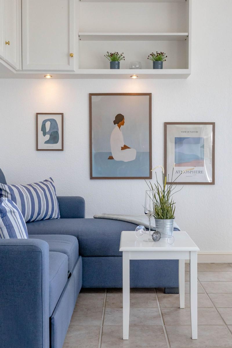 Ein Wohnzimmer mit blauem Sofa, weißen Möbeln und Bildern an der Wand.