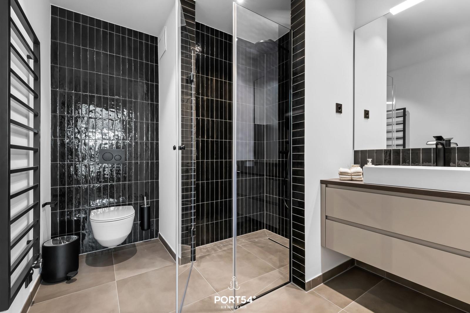 Moderne Badewanne mit Dusche, Toilette und Waschtisch. Schwarze Fliesen und Spiegel.