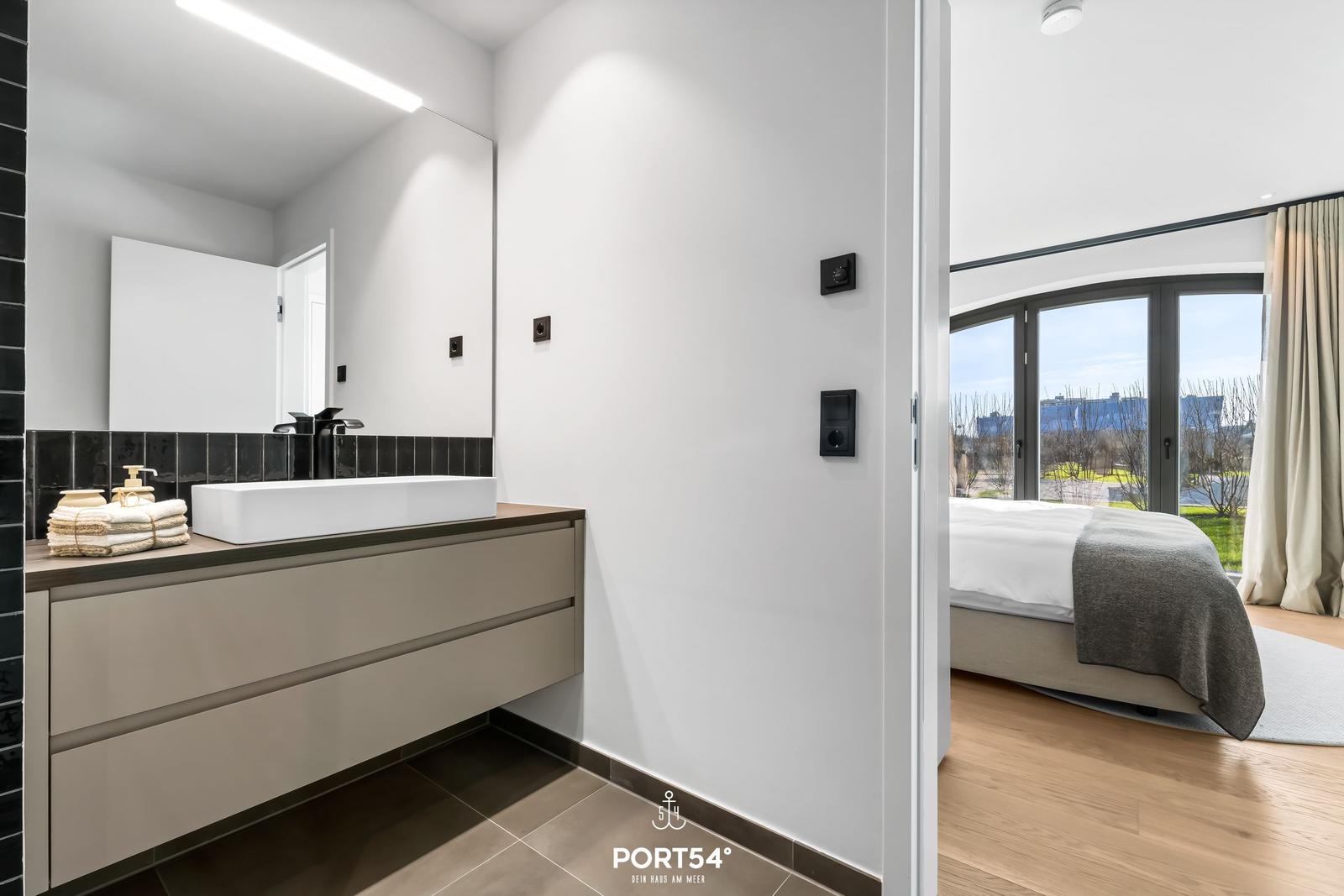 Badezimmer mit Waschtisch und Spiegel. Schlafzimmer mit Bett und Fenster.