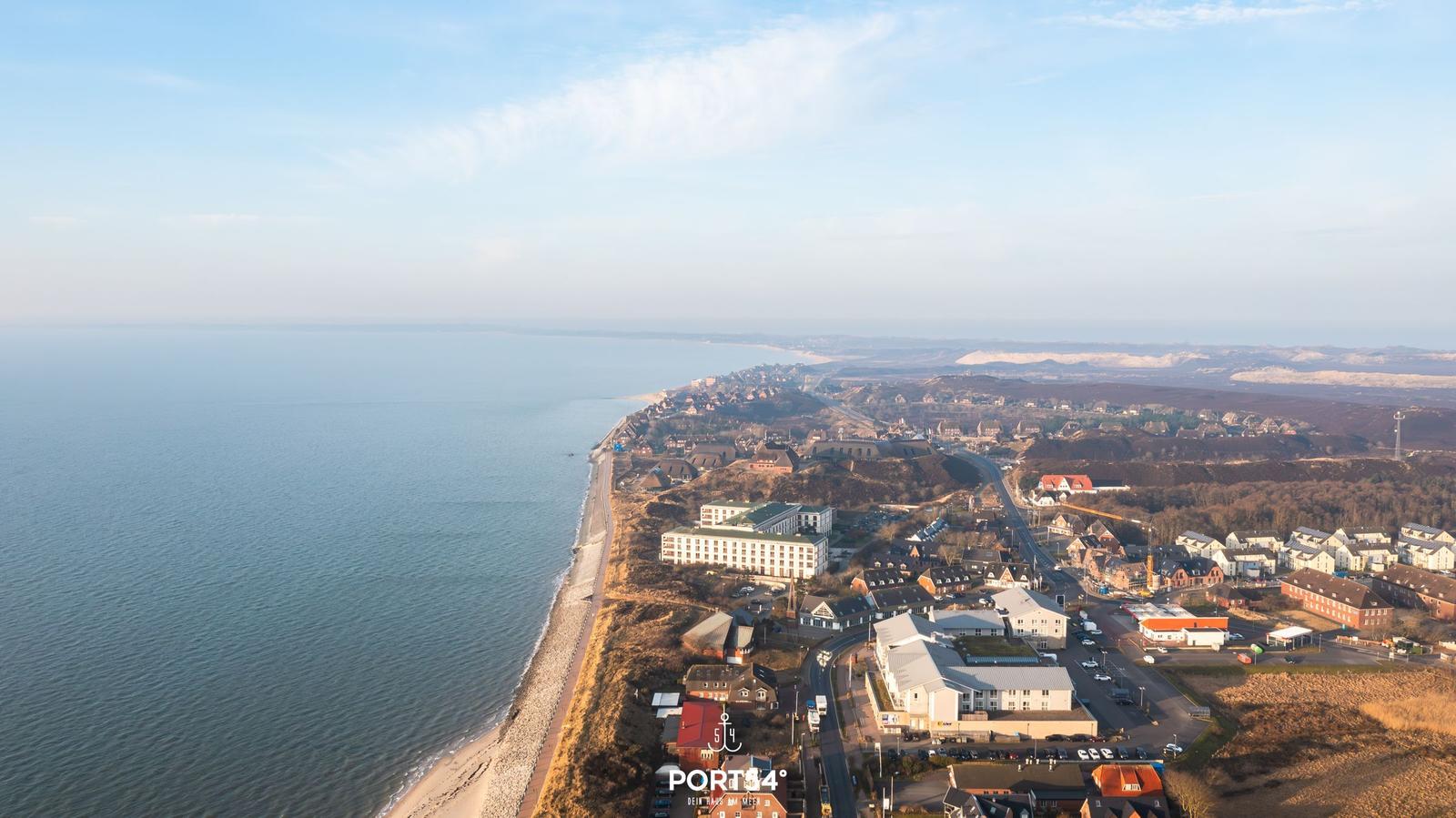 Aerial view of coastal town with beach, houses, and distant dunes.