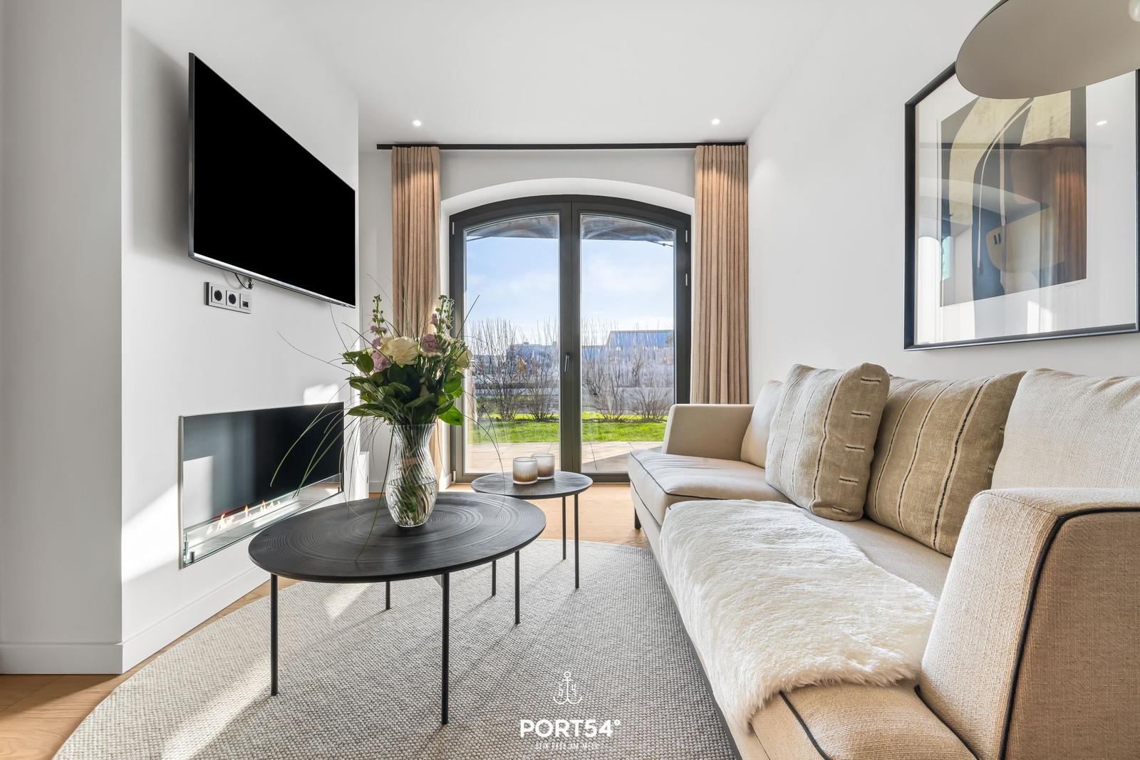 Wohnzimmer mit Sofa, Fernseher und Blick auf die Terrasse.