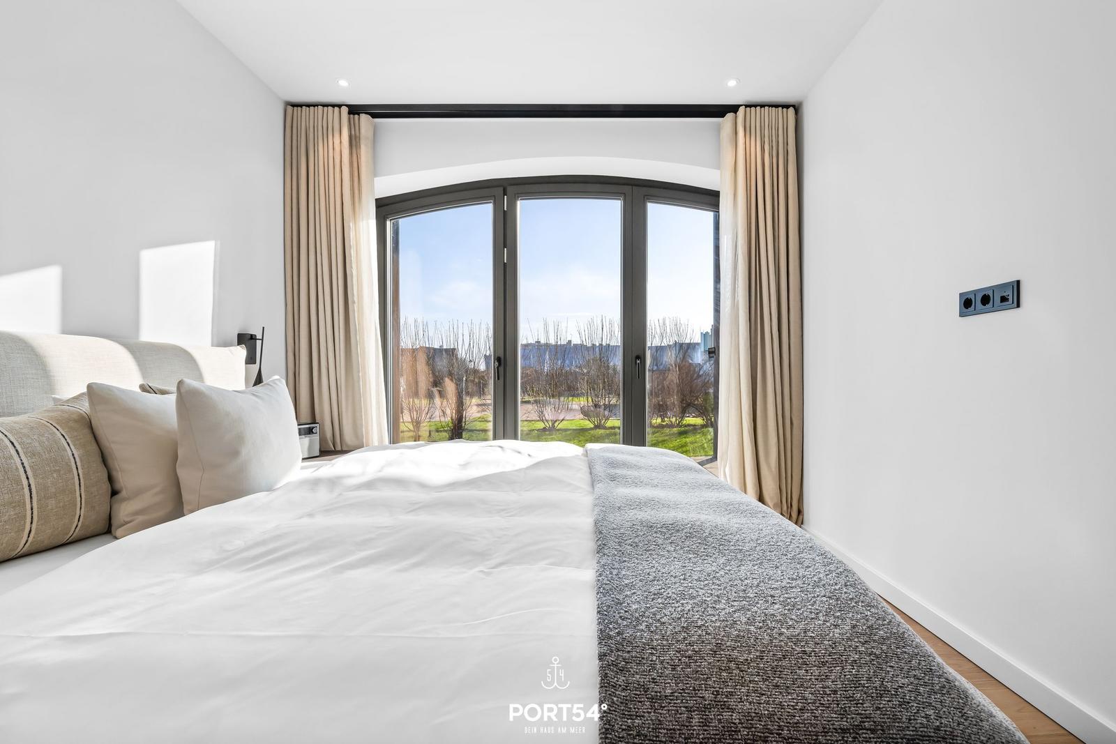 Schlafzimmer mit großem Bett und Bogenfenster zur Außenterrasse.