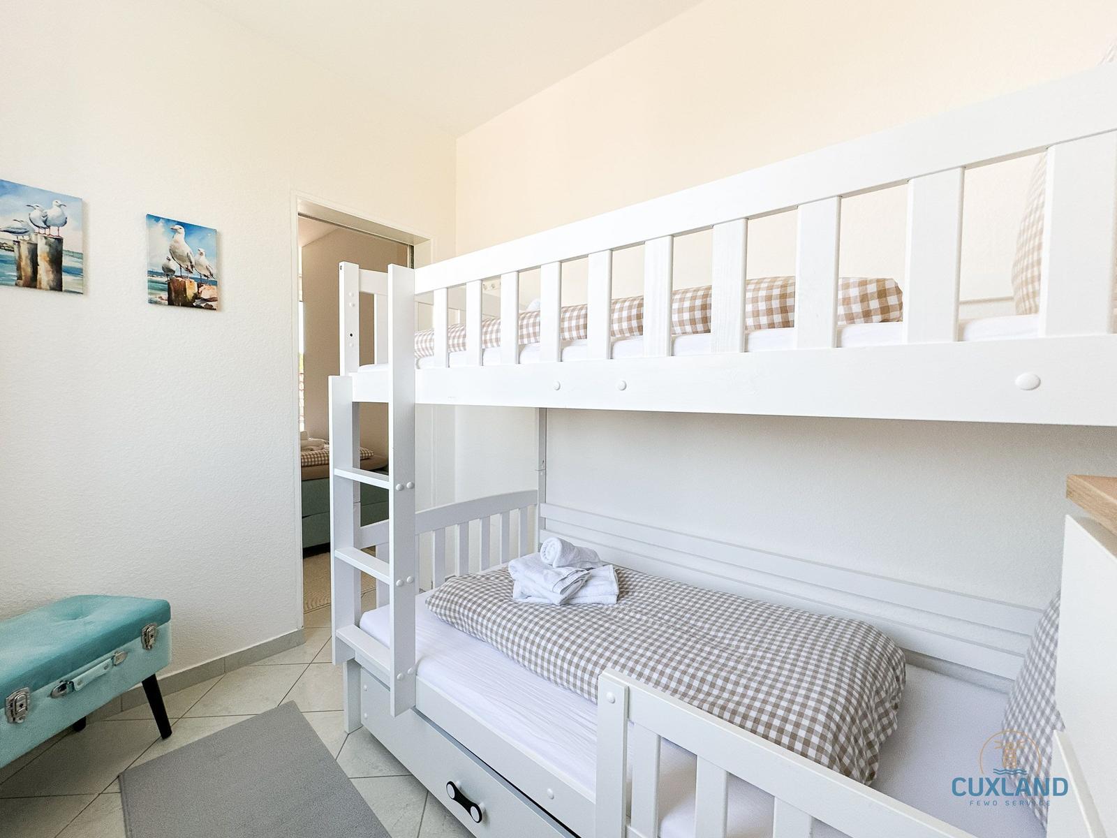 Zimmer mit Doppelstockbett, Kissen und Handtüchern. Wandbilder und blauer Sitzbank.