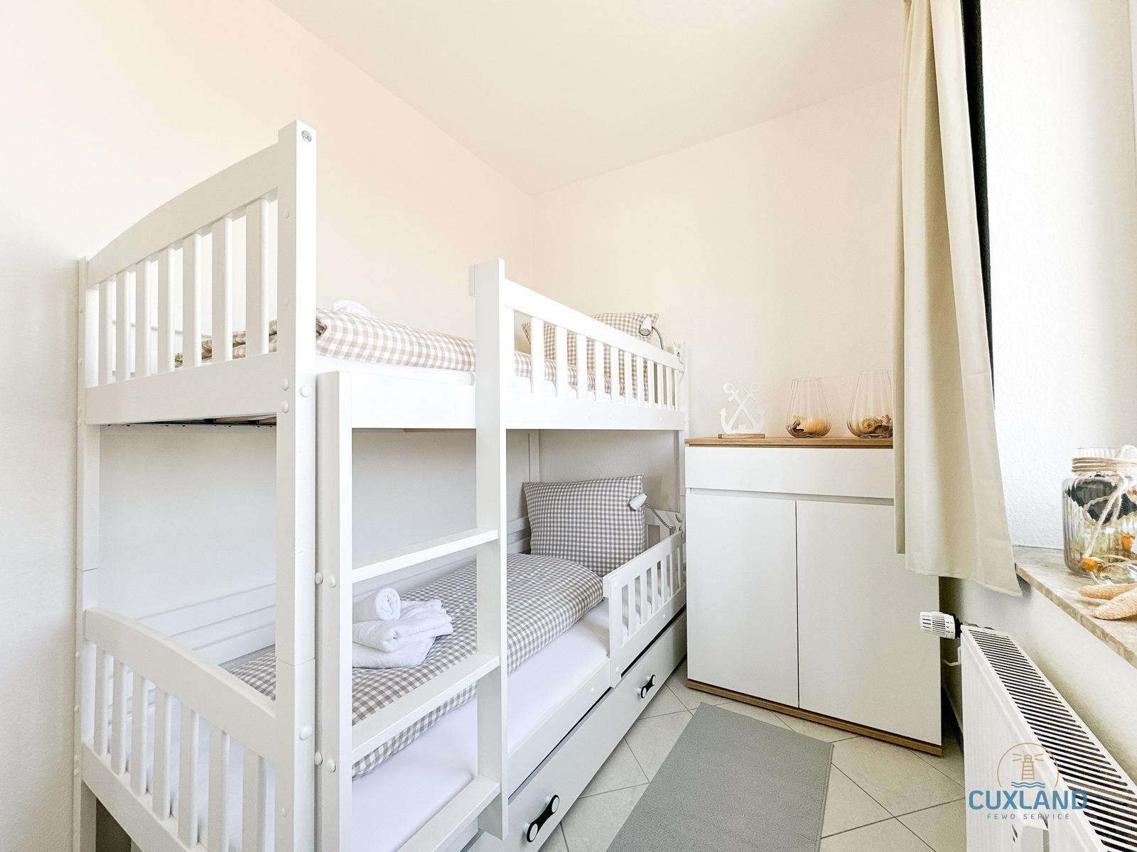 Zimmer mit Doppelstockbett, Schrank und Fenster mit Vorhang.
